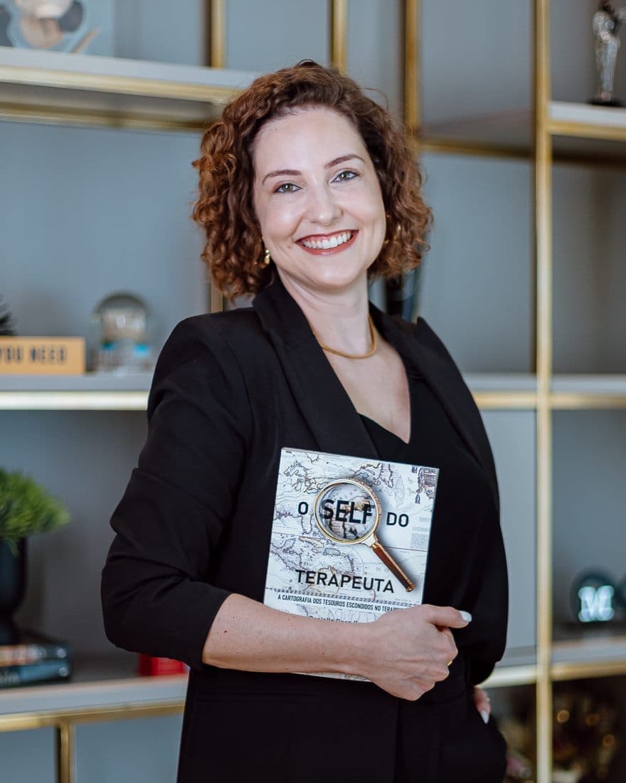 Danielle Doss Damo com O Self do Terapeuta, livro de sua autoria, na estante do instituto.